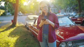 Woman is standing outdoors near the red vintage car and using smartphone
