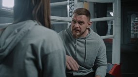 Female fighter sits on ring and talks with male coach about match. Trainer consults woman and explains fighting technique. Fighter prepares to competition in gym. Physical activity and workout. - Powered by Shutterstock - Get 15% off with code: PIKWIZARD15
