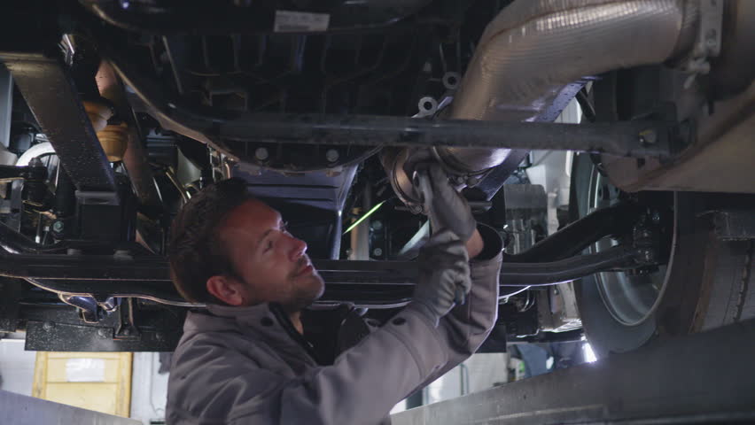 Mechanic repairing underneath truck and looking at camera. Smiling young handsome mechanic using wrench while working under lifted vehicle portrait Royalty-Free Stock Footage #3425682831