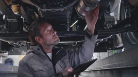 Mechanic examining trailer vehicle underbody part and using digital tablet. Repairman checking pipe under truck in auto repair station - Powered by Shutterstock - Get 15% off with code: PIKWIZARD15