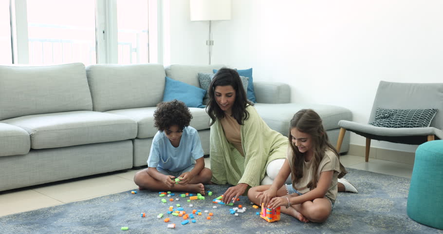 Positive caring Latin mom and two children playing creative family game at home together, constructing towers from colorful cubes, sitting on heating carpeted floor in living room Royalty-Free Stock Footage #3425702717