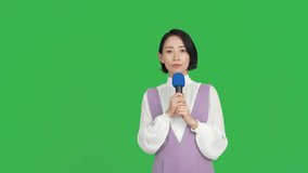 An Asian reporter reporting with a microphone. Green background for chroma key composition.