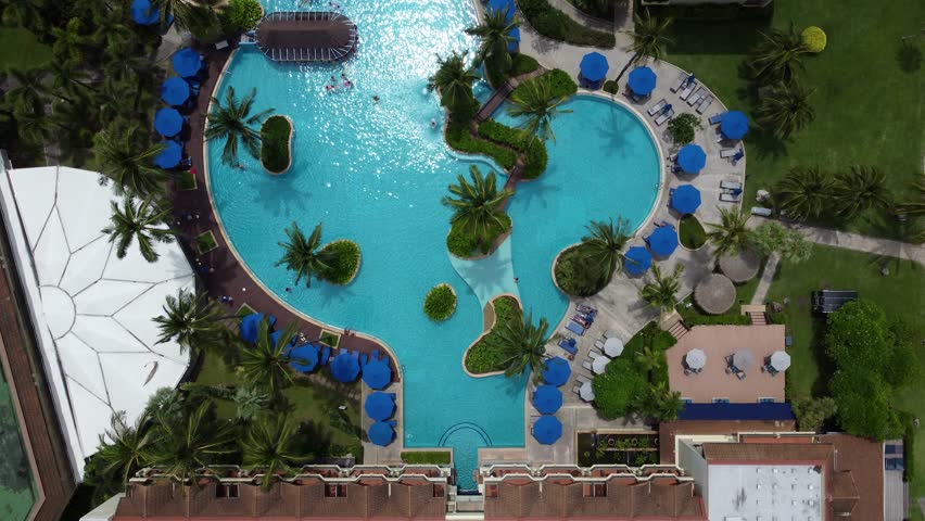Aerial top down view of 5-star hotel swimming pool people swim sun tan and play also showing blue parasols and palm trees and the rooms on the side of the aquatic facility 4k high resolution quality Royalty-Free Stock Footage #3425713803