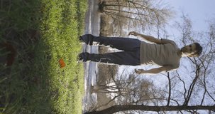 Vertical video of young skinny fit man doing exercise in park jumping on a bright sunny day looking serious alone