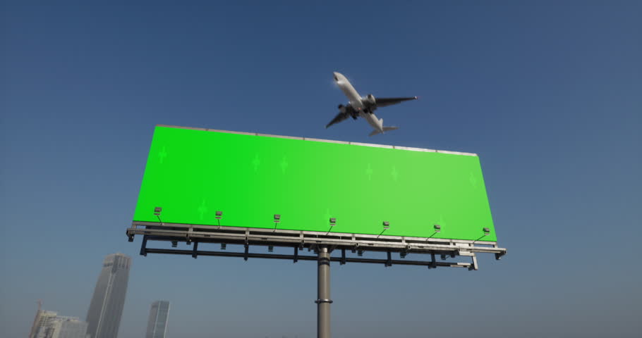 Large airliner with passengers on blue clear sky is landing at airport of bright on sunny summer day. A cargo plane flies over a billboard with chromakey by the road