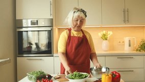 Happy elderly Caucasian 60s woman preparing vegetable meal, smiling vegetarian girl cooking healthy food salad using cookbook menu in modern kitchen - Powered by Shutterstock - Get 15% off with code: PIKWIZARD15