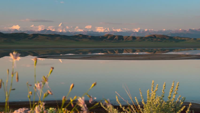 Early quiet morning on a mountain lake. The surface of the lake reflects the snow-capped mountains on the horizon. Lake Tuzkol. Kazakhstan. Time lapse