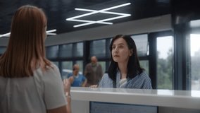 Adult woman stands near reception desk in clinic lobby area and comes to appointment with doctor. Female administrator talks with patient at information counter. Medical staff work in modern hospital. - Powered by Shutterstock - Get 15% off with code: PIKWIZARD15