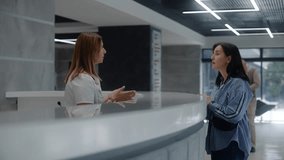 Adult woman stands at reception desk in clinic lobby entrance and makes appointment with doctor. Female administrator talks with patient at information counter. Medical staff work in modern hospital. - Powered by Shutterstock - Get 15% off with code: PIKWIZARD15
