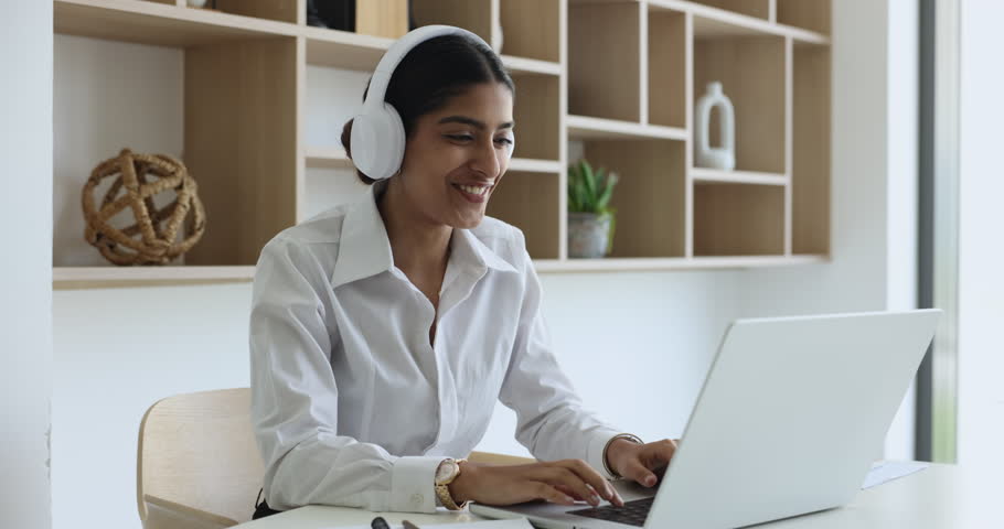 Positive beautiful young Indian manager woman in headphones talking on online video conference call, speaking at laptop screen, smiling, enjoying internet business communication Royalty-Free Stock Footage #3426198411