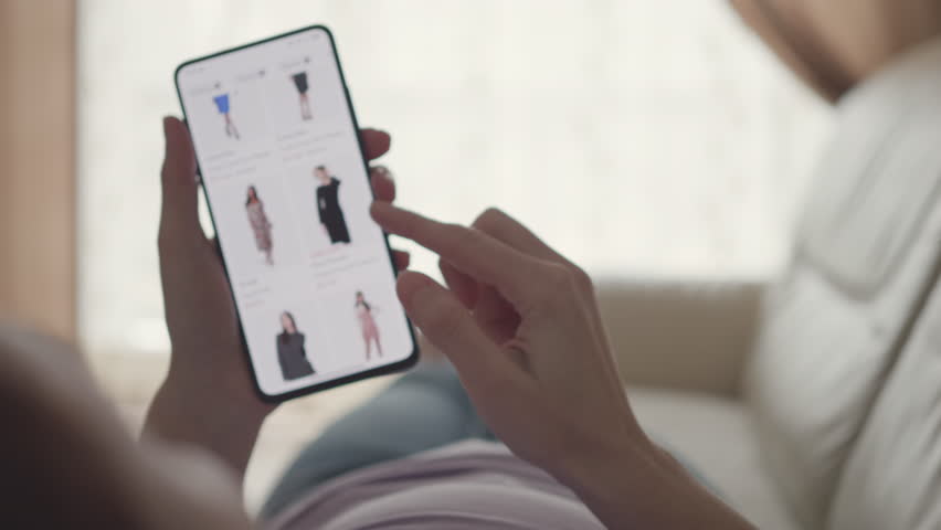 Woman at Home Lying on Couch in Living Room Using Smartphone. Woman Looks at Goods in Online Store Clothing. Buy Fashion Clothes Directly on Smartphone. Buying in Online Store Using in Smartphone. 
