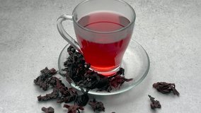 Red hibiscus tea in a glass cup and dried hibiscus flowers on the table
