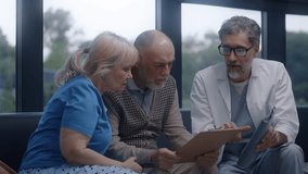 Elderly couple sits on sofa in clinic lobby area after appointment with doctor. Doctor talks, discusses medical examination or test results. Waiting room in modern medical center. Healthcare system. - Powered by Shutterstock - Get 15% off with code: PIKWIZARD15