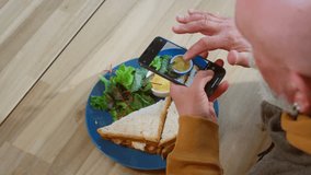 The old man takes a photo of breakfast on his smartphone. A pensioner takes a photo of food on a phone camera for social networks. An old man holds a gadget with his hands. Street food and sandwiches - Powered by Shutterstock - Get 15% off with code: PIKWIZARD15