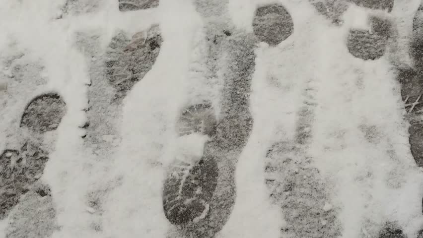 Footprints on white snow. Drive along the asphalt road, on which there is fresh, recently fallen snow. Black footprints of the shoes of people who recently passed here are imprinted in the white snow.
