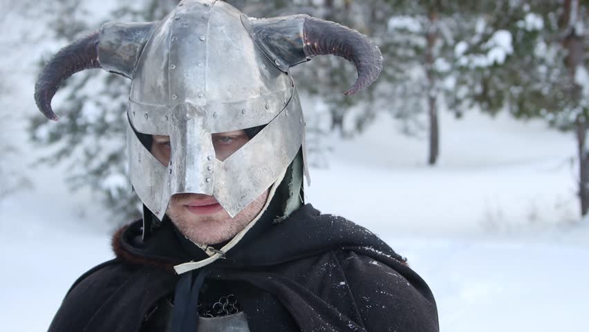 Portrait of a medieval fantasy warrior in a horned helmet, steel breastplate, chainmail with a two-handed ax in his hands, posing against the backdrop of a winter forest. Camera movement.