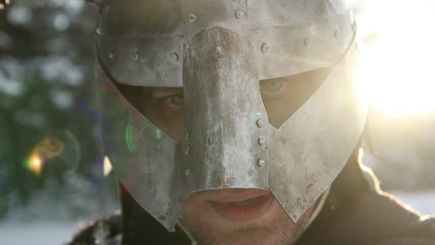 Medieval fantasy warrior in a horned helmet, posing against the backdrop of sunset in a winter forest. Rays of the sun, glare. Camera movement, selective focus.