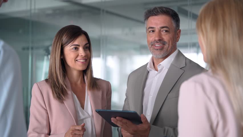 Smiling busy mature business man and business woman professional corporate executive leaders managers discussing digital strategy using tablet computer in office working with team. - Powered by Shutterstock - Get 15% off with code: PIKWIZARD15