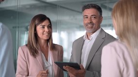 Smiling busy mature business man and business woman professional corporate executive leaders managers discussing digital strategy using tablet computer in office working with team. - Powered by Shutterstock - Get 15% off with code: PIKWIZARD15