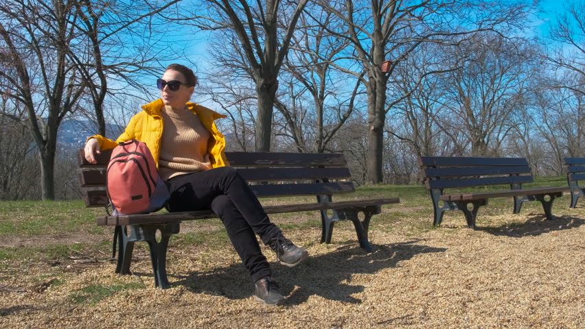 Lady leisure activity alone on bench. A nice young lady with backpack have a leisure on the bench against spring park.