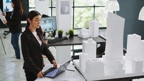 Asian contractor takes notes about 3d printed model on laptop, examining outline and scale of building maquette in architectural agency office. Cad specialist measuring layout for new project. - Powered by Shutterstock - Get 15% off with code: PIKWIZARD15