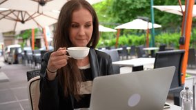 Young adult woman drinking tea and working with laptop computer on restaurant terrace.