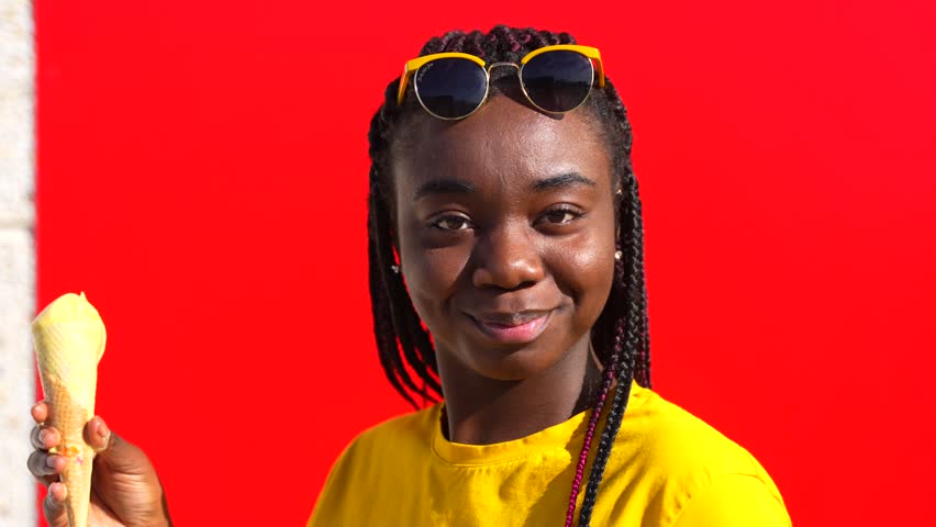 Happy young african woman eating an ice cream leaning on a red wall