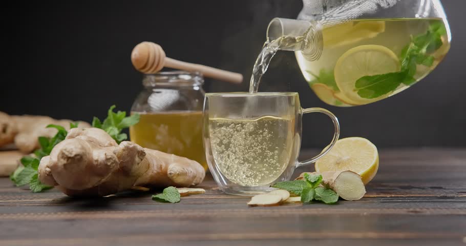 hot steaming organic herbal tea with ginger, mint and lemon pours in a glass cup on a wooden table