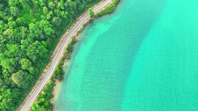 A stunning tropical coastal road, captured from above, winding its way through vibrant green coastal paradise, touching the azure sea. Traffic and nature concept. Ko Chang island, Thailand. 4K HDR. 
