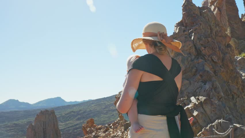 Young mother holding baby in majestic landscape of Tenerife, back view