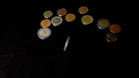 Two euro coin rotates on a black table. Handful of coins lies nearby in the background. Concept of the circulation of money, investment, savings, pension, rich life. - Powered by Shutterstock - Get 15% off with code: PIKWIZARD15