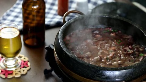 Delicious feijoada served in a stone pot typical of Minas Gerais on a rustic wooden table accompanied by seasonings. Traditional Brazilian food.
