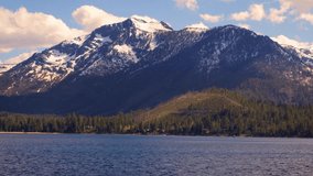 A speedboat cruises on Lake Tahoe with forests and snowy Sierra Nevada Mountains in the background. 4K UHD video.