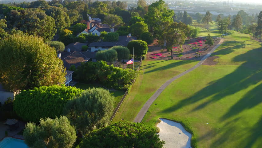 Aerial: Panning Shot Of Residential Roofed Houses Amidst Green Trees, Drone Flying Over Green Golf Course On Sunny Day - Long Beach, California