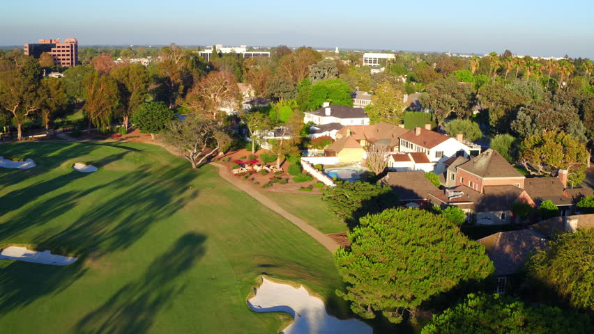 Aerial: Tilt Down Shot Of Swimming Pools Outside Roofed Houses, Drone Flying Forward Over Golf Course On Sunny Day - Long Beach, California
