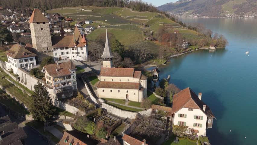 Spiez castle and church with Lake Thun and Swiss Alps in the background, clear day, aerial view