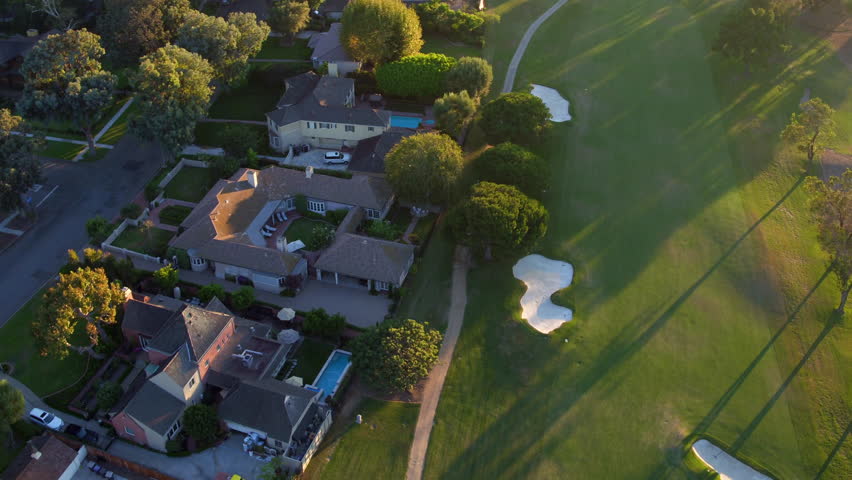 Aerial Panning Shot Of Swimming Pools Outside Roofed Houses, Drone Flying Over Green Golf Course - Long Beach, California