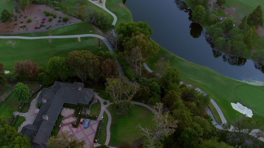 Aerial: Drone Panning Tilt Up Shot Of Pond In Golf Course Amidst Houses At Sunset - Long Beach, California