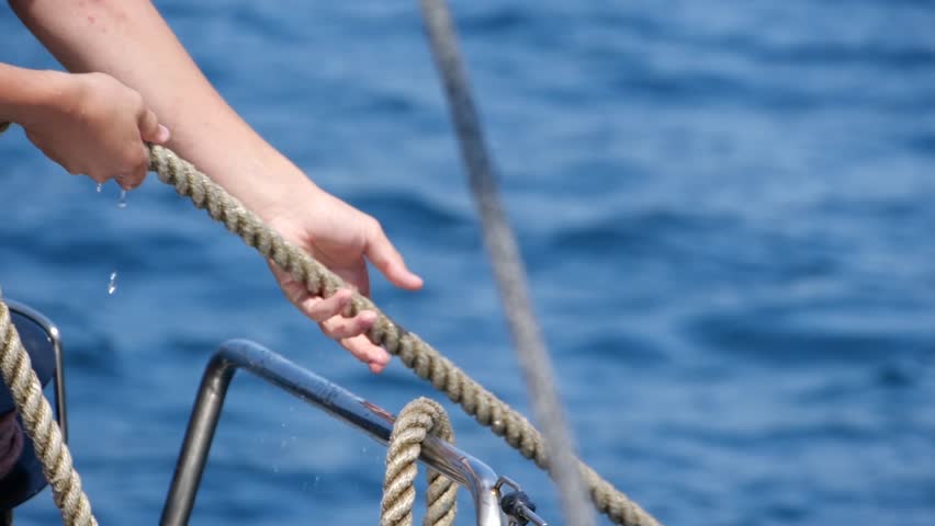 Close up of man pulling ropes during sailing, winding sheets around winches. Sailor mans hand pulling grey rope. Sailing trip on mediterranean sea. Slow motion footage