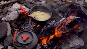 Vertical video of roast sausage and boiling water over bonfire at cold night. Fast dinner camping in countryside. Camping utensils. 