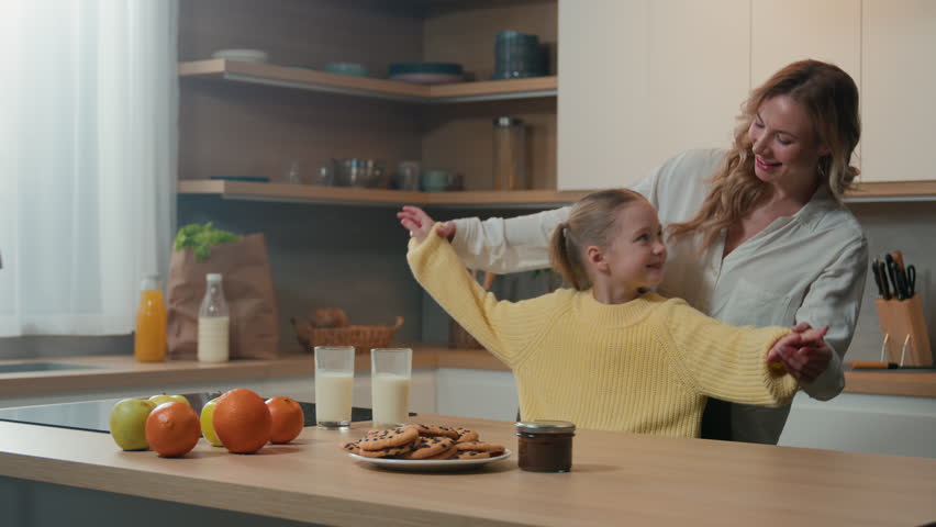 Happy carefree smiling mother and little daughter at kitchen having fun hold hands dancing to music moving dance mom with child girl hug kid hugging embracing cuddling family breakfast love bonding Royalty-Free Stock Footage #3427104013