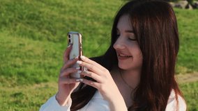 Young woman shoots video on smartphone against field. Smiling lady uses modern gadgets to keep memories about summer holidays