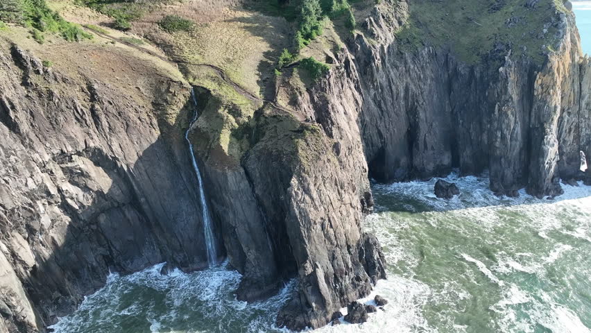 A narrow waterfall flows off an impressive cliff near the Neahkahnie Viewpoint along the Oregon coast. This Pacific Northwest region, where forest meets the sea, is home to stunning coastlines.