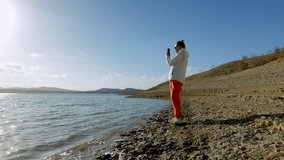 A woman is on a rocky shore and takes a video on her smartphone. Hiking concept.