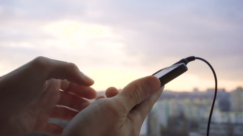 Detail of stereo jack being plugged into smartphone with sunset on background