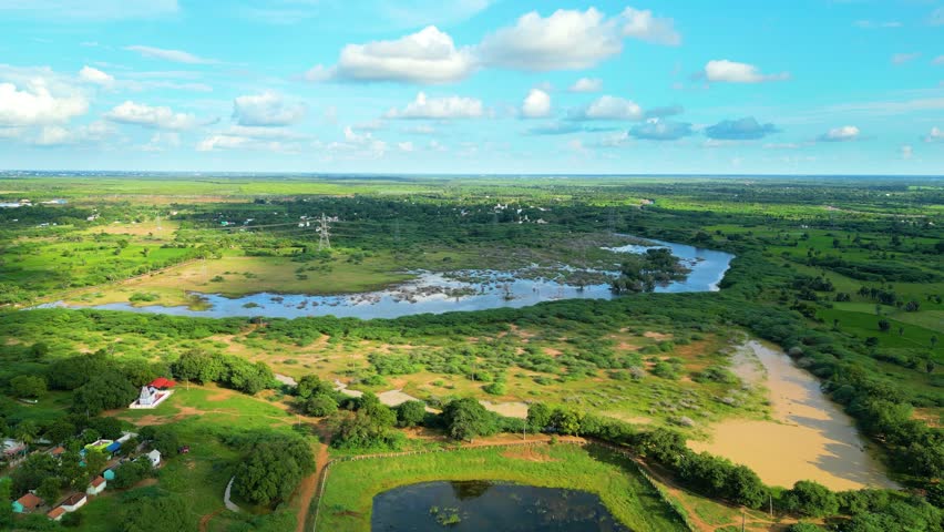 Lush green landscape with winding river, clouds casting shadows, sunny day, aerial view
