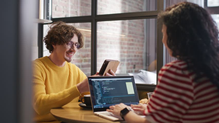 Cute Caucasian couple discussing something at kitchen table. Woman typing in code as part of her work while husband found positive information on laptop. Creating new software for project.