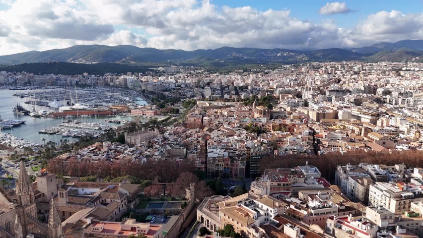 Aerial establishing shot showing Beautiful historic city of Palma de Mallorca with harbor and sailing boats - Mountain range of island in background - Spanish neighborhood in capital
