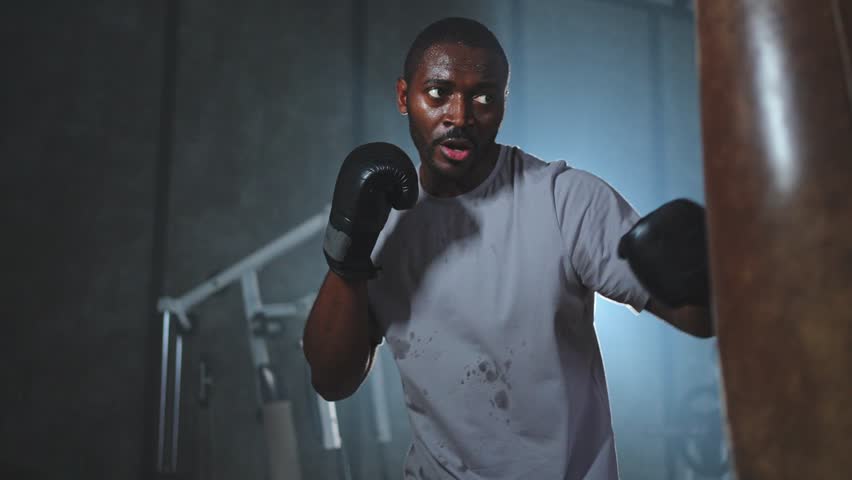 Fitness workout in gym. Strong African man fighter training punches with boxing bag. Healthy boxer man punching boxing bag in gym. Training day in boxing gym. Strength fit body workout training Royalty-Free Stock Footage #3427327183