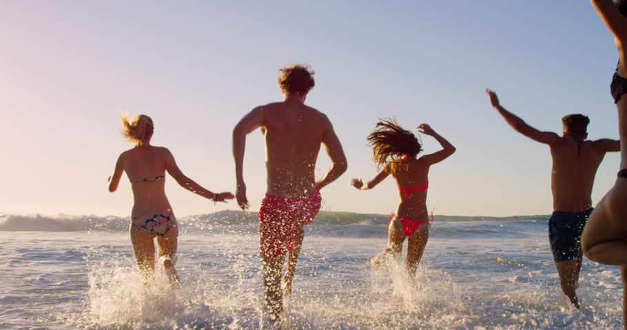 Beach, wave and friends playing in ocean together for fun on travel, vacation or holiday in summer. Splash, back and group of young people in sea or water outdoor on tropical coast for getaway